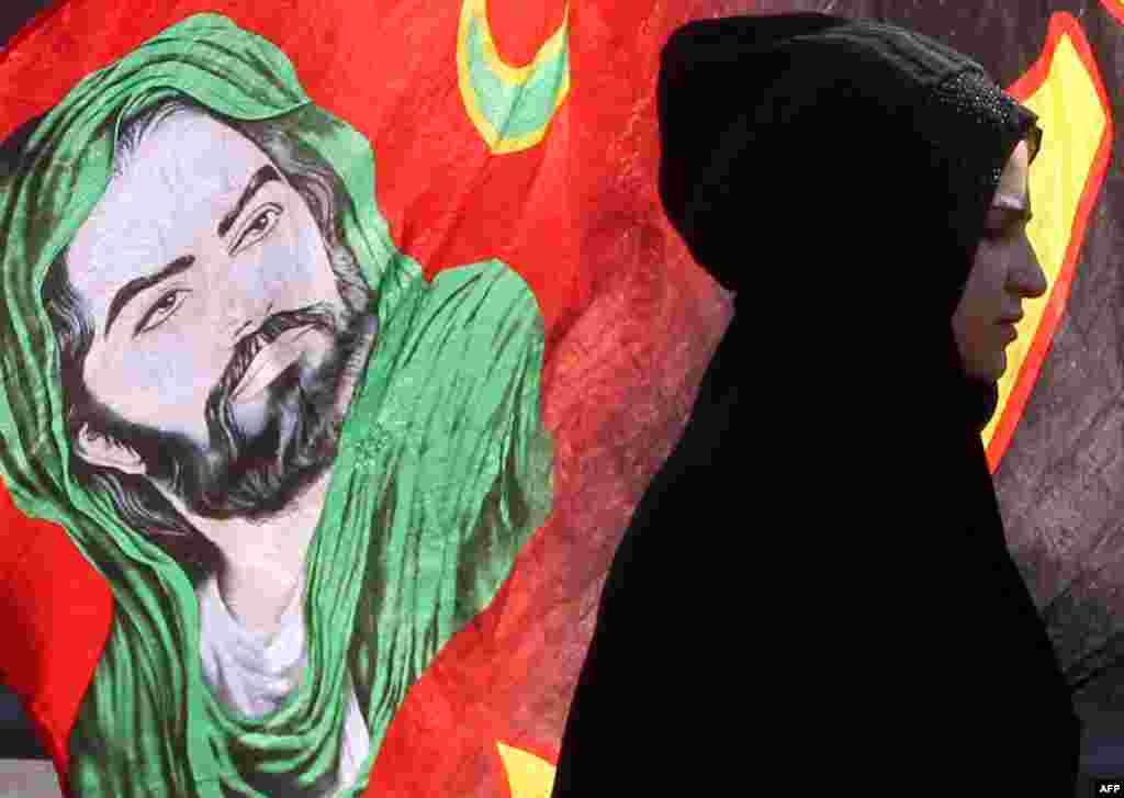 Seorang peziarah Muslim Syiah Irak berjalan melewati spanduk bergambar Imam Hussein sepanjang jalan utama yang menghubungkan Baghdad dengan kota Karbala, untuk berpartisipasi dalam festival keagamaan Arbaeen. 