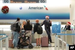 American Airlines employees, some wearing Santa Claus hats, check in travelers in the American terminal at Miami International Airport, on Christmas Eve, Dec. 24, 2024, in Miami, Florida.