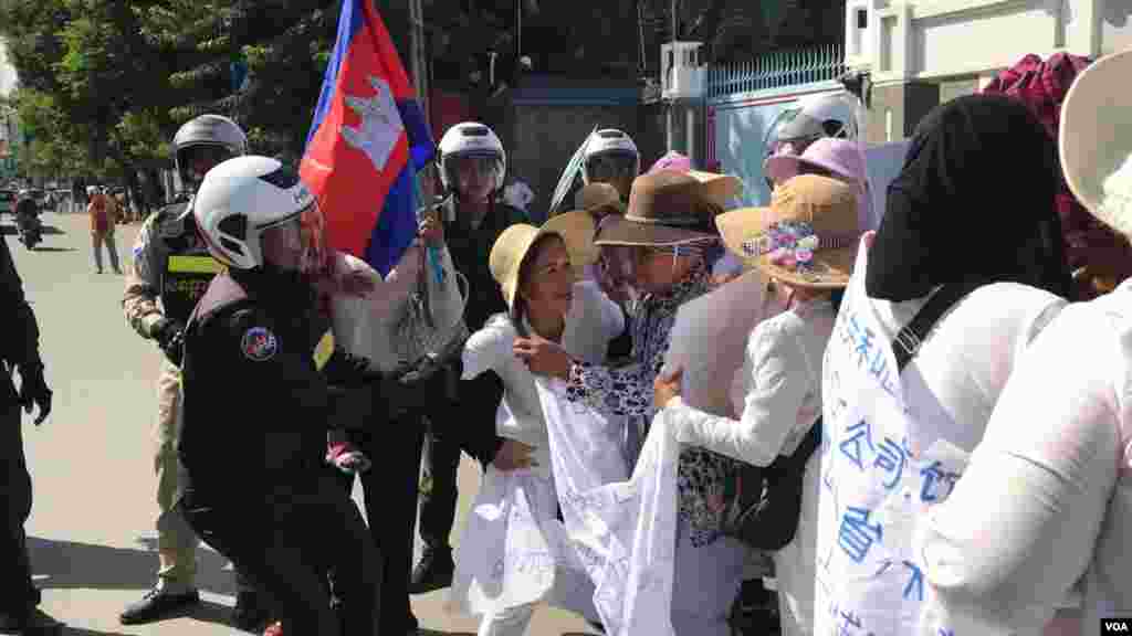 ក្រុម​សន្តិសុខ​កំពុង​ទាញ​ និង​អូស​ប្រជា​​ពលរដ្ឋ​​​មាន​ទំនាស់​ដី​ធ្លី​ជាមួយ​​ក្រុមហ៊ុន​ចិន ​Union Dev​el​o​pm​ent Group (UDG) ដែល​តវ៉ាសុំ​អន្តរាគមន៍​​នៅ​មុខ​ស្ថាន​ទូត​ចិន​ ​ ​​ចេញ​ពីស្ថានទូត​ នា​ថ្ងៃទី​១៣ ខែសីហា​ ឆ្នាំ​២០១៩។ (កាន់ វិច្ឆិកា/VOA) 