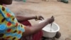 A mother cooking porridge for her children in Dowa district, Malawi. In some families the new school home feeding programs is helping suppliment family food. (Lameck Masina/VOA)