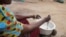 A mother cooking porridge for her children in Dowa district, Malawi. In some families the new school home feeding programs is helping suppliment family food. (Lameck Masina/VOA)