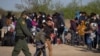 A U.S. Border Patrol Agent escorts two asylum-seeking unaccompanied minors from Central America as others take refuge near a baseball field after crossing the Rio Grande river into the United States from Mexico on rafts, in La Joya, Texas, March 19, 2021.
