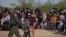 A U.S. Border Patrol Agent escorts two asylum-seeking unaccompanied minors from Central America as others take refuge near a baseball field after crossing the Rio Grande river into the United States from Mexico on rafts, in La Joya, Texas, March 19, 2021.