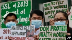 FILE - Health workers wearing protective masks hold signs during a rally outside a hospital in metropolitan Manila, Philippines, Feb. 7, 2020, demanding the government ensure their safety and raise their pay amid to the coronavirus threat.