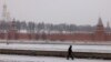FILE - A pedestrian walks along an embankment of the Moskva river with the Kremlin on the background during a snowfall in Moscow, Jan. 21, 2022. 