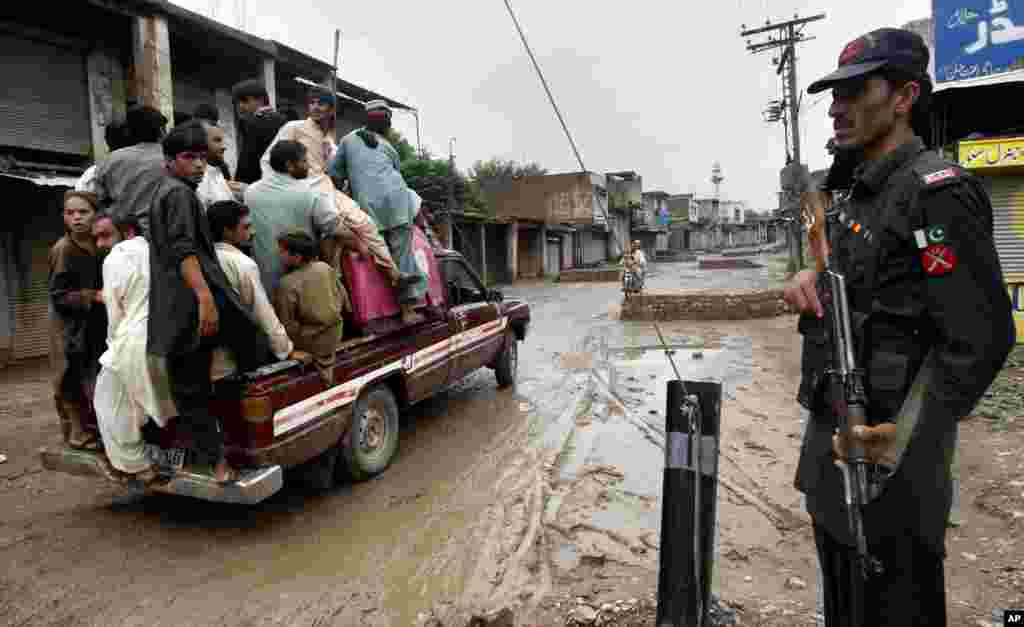 A Pakistani paramilitary soldier stands guard at a checkpoint as people on a pickup truck head to their village after authorities reopen the road in Bara, a town in the Pakistan Khyber Tribal region along the Afghan border, August 3, 2013.