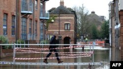 A woman walks on a raised walkway over floodwater after the River Ouse burst its banks in York, northern England, Feb. 17, 2020, in the aftermath of Storm Dennis.