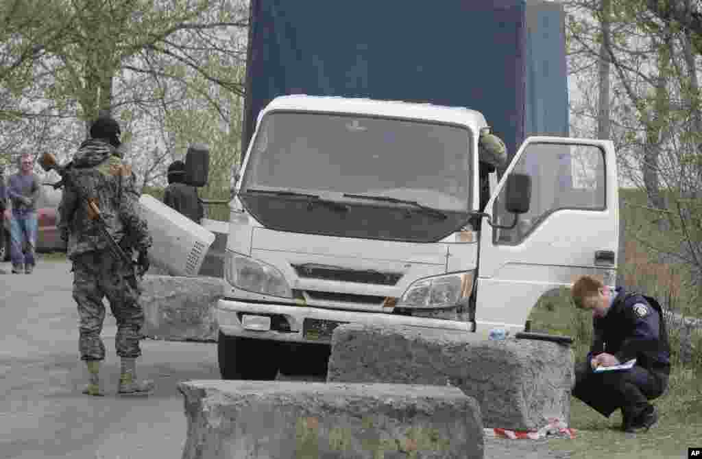 Seorang pria bersenjata pro-Rusia mengamati polisi (kanan) saat ia menginspeksi sebuah daerah menyusul pertempuran di sebuah pos pemeriksaan yang dikontrol para aktivis pro-Rusia di desa Bulbasika, Ukraina (20/4). (AP/Efrem Lukatsky)