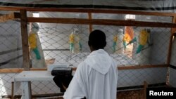 FILE - A priest watches as health workers dressed in Ebola protective suits prepare the body of an Ebola patient for burial at the Ebola treatment center in Butembo, in the Democratic Republic of Congo, March 26, 2019. 