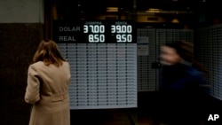 一位女子在阿根廷布宜诺斯艾利斯街头的汇率牌上查看美元对巴西里尔和阿根廷比索的汇率。2018年9月3日。