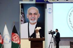 FILE - Backdropped by his own image, Afghan President Ashraf Ghani speaks to delegates during the first day of the Afghan Loya Jirga meeting in Kabul, Afghanistan, April 29, 2019.