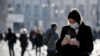 A woman wearing a sanitary mask looks at her phone in Milan, Italy, Monday, Feb. 24, 2020. 