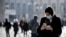 A woman wearing a sanitary mask looks at her phone in Milan, Italy, Monday, Feb. 24, 2020. 