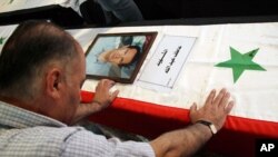 A Syrian man mourns a relative whose picture is displayed atop his coffin with Arabic words that read: "The Martyr, Atef Abdullah" during a mass funeral procession for several Syrians killed in a twin suicide bombings, at a mosque in Damascus, Syria Satur