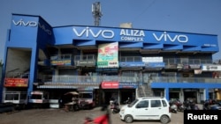 资料照：2018年12月14日，在印度艾哈迈达巴德，一名摩托车手骑过一家购物中心，旁边挂着中国智能手机制造商Vivo的广告牌，（路透社）