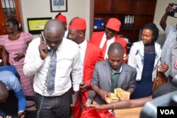 On phone, an officer in the Parliament Accounts office makes frantic calls as members of the opposition storm the office to return $8000 given to them to consult on the Age Limit, Oct. 25, 2017. (Halima Athumani for VOA)