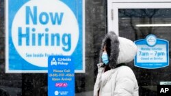 រូបឯកសារ៖ ស្ត្រីម្នាក់ដើរកាត់ហាងលក់ទំនិញមួយដែលមានបិទបដា «រើសបុគ្គលិក» ក្នុងទីក្រុង Schaumburg រដ្ឋ Illinois សហរដ្ឋអាមេរិក កាលពីថ្ងៃទី ៦ ខែកុម្ភៈ ឆ្នាំ ២០២១។