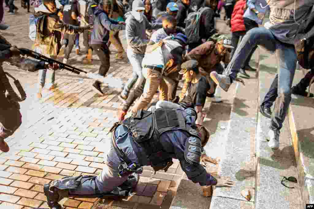 The flash of an exploding stun grenade is seen as a student from the University of Witwatersrand jumps on a falling policeman while another policeman fires rubber bullets from his rifle during a mass demonstration on campus in Johannesburg, South Africa, Oct. 4, 2016. Authorities tried to re-open the prestigious Wits University after weeks of demonstrations.