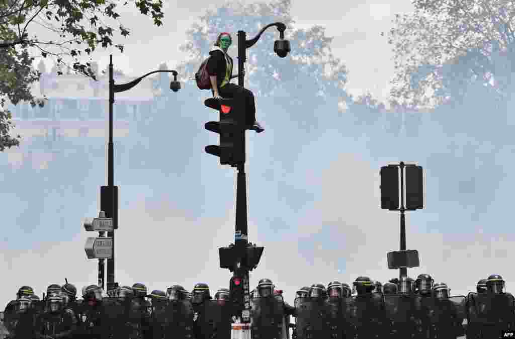 A demonstrator with the face painted in green, sits on a traffic light as French riot police secure the area during a protest against the controversial labor reforms of the French government in Paris, Sept.15, 2016.