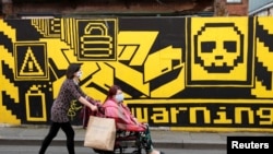 People wearing protective face masks walk down the street, as the city and surrounding areas face local restrictions in an effort to avoid a local lockdown being forced upon the region, in Manchester, Britain, Aug. 3, 2020.