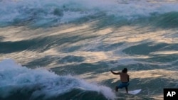FILE - A surfer rides a wave as the color of the sky is reflected on the water in Navarre Beach, Fla., Monday, June 17, 2024. (AP Photo/Kiichiro Sato)