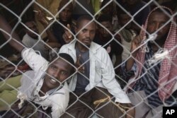 Ethiopian migrants look through a fence as they wait to be evacuated at a departure center in the western Yemeni town of Haradh, on the border with Saudi Arabia and Yemen, Wednesday, March 21, 2012.