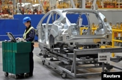 FILE - An employee uses a laptop next to a car body at an assembly line at a Ford manufacturing plant in Chongqing municipality, April 20, 2012.