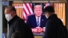 Masked people walk in front of a TV screen showing a live broadcast of U.S. President Donald Trump's speech at the Seoul Railway Station in Seoul, South Korea, March 12, 2020. 