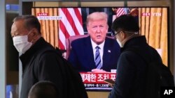 Masked people walk in front of a TV screen showing a live broadcast of U.S. President Donald Trump's speech at the Seoul Railway Station in Seoul, South Korea, March 12, 2020. 