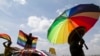 FILE - A person holds an umbrella bearing the colors of the rainbow flag as others wave flags during a gay pride rally in Entebbe, Uganda, Aug. 9, 2014. 