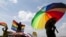 FILE - A person holds an umbrella bearing the colors of the rainbow flag as others wave flags during a gay pride rally in Entebbe, Uganda, Aug. 9, 2014. 