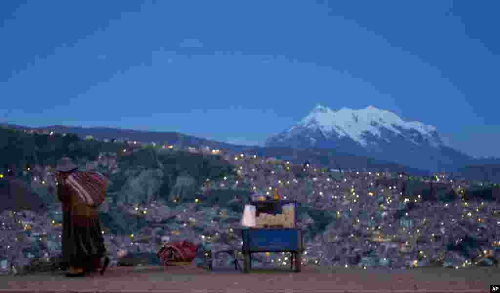 ស្រ្តី​ម្នាក់​ដើរ​តាម​ដងផ្លូវ​ Pereferica Avenue កាត់​តូប​លក់​ពោតលីង​មូយ​ ហៅ​ថា&laquo;pipocas&raquo; ដោយ​មាន​ភ្នំ Illimani Mountain​ នៅ​ខាងក្រោយ​អំឡុង​ពេលព្រះអាទិត្យ​លិច​នៅ​ក្នុង​ទីក្រុង​ La Paz ប្រទេស​បូលីវី។