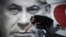 A woman takes part in a protest against Israeli Prime Minister Benjamin Netanyahu, seen on the poster, in Tel Aviv, Israel, April 19, 2020.