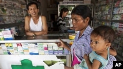 This Aug. 26, 2009 photo shows a merchant in Pailin, Cambodia speaking with a woman as she holds her sick child at a drug store. Posters with message: “Counterfeit medicine kills, while real medicine heals” will be distributed to public hospitals, health 