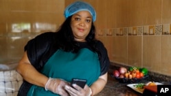 Anita Akpeere, who uses her mobile phone to run her business, stands inside her restaurant in Accra, Ghana, Tuesday, April 23, 2024. (AP Photo/ Misper Apawu)
