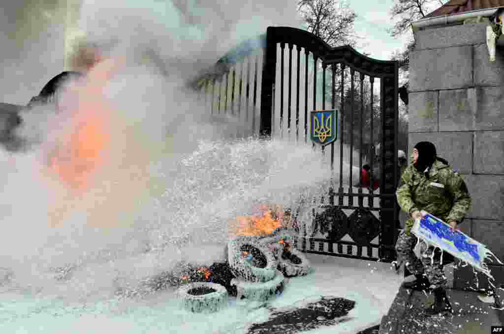 A Ukrainian serviceman throws a signboard over the gates as the flames are doused after fighters of the Aydar Ukrainian volunteer battalion, burn tires at the entrance to the Ukrainian Defense Ministry in Kyiv, Feb. 2, 2015, to prevent the possible disbandment of their battalion.
