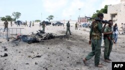 Petugas keamana Somalia berjalan melewati mobil yang hancur akibat ledakan bom di gedung parlemen di luar gedung parlemen Somalia di Mogadishu (5/7).