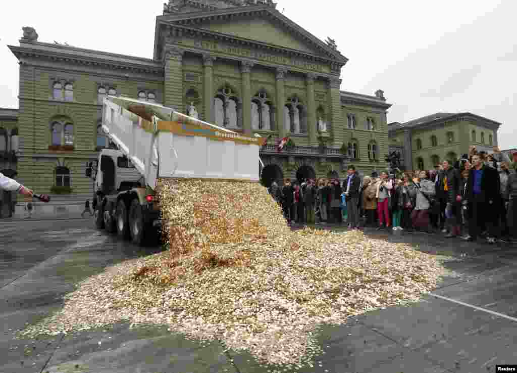 Sebuah truk menumpahkan koin-koin lima Rappen di Lapangan Federal dalam aksi Komite Inisiatif "CHF 2500 perbulan untuk setiap orang" (Gundeinkommen) di Bern, Swiss. Komite tersebut mengirimkan 126.000 tandatangan kepada Kanselir untuk mengusulkan perubahan pada konstitusi untuk melaksanakan inisiatif mereka yang bertujuan untuk mendapatkan pembagian pemasukan rumahtangga bulanan sebesar CHF 2.500 (US$ 2700) dari pemerintah untuk setiap warga negara Swiss yang tinggal di Swiss. 