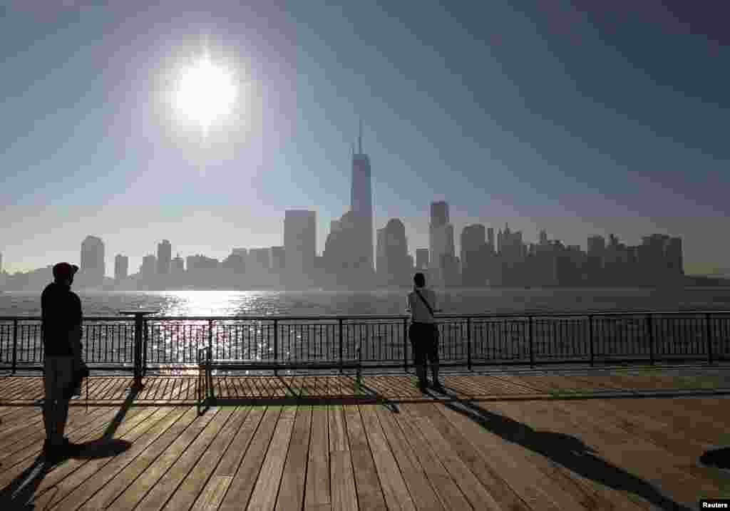 Dua orang di Jersey City, New Jersey, terlihat memandang cakrawala kota New York di seberang&nbsp; Sungai Hudson, setelah potongan terakhir, yang merupakan puncak dari One World Trade Center terpasang. 