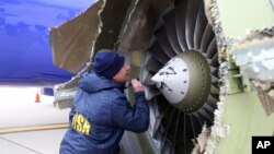 A National Transportation Safety Board investigator examines damage to the engine of the Southwest Airlines plane that made an emergency landing at Philadelphia International Airport in Philadelphia, April 17, 2018. (NTSB via AP)