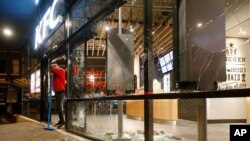 FILE - A man rests on his broom as he stands next to shards of glass and smashed windows of a restaurant that was damaged in protests against a nationwide coronavirus curfew in Rotterdam, Netherlands, Jan. 25, 2021.