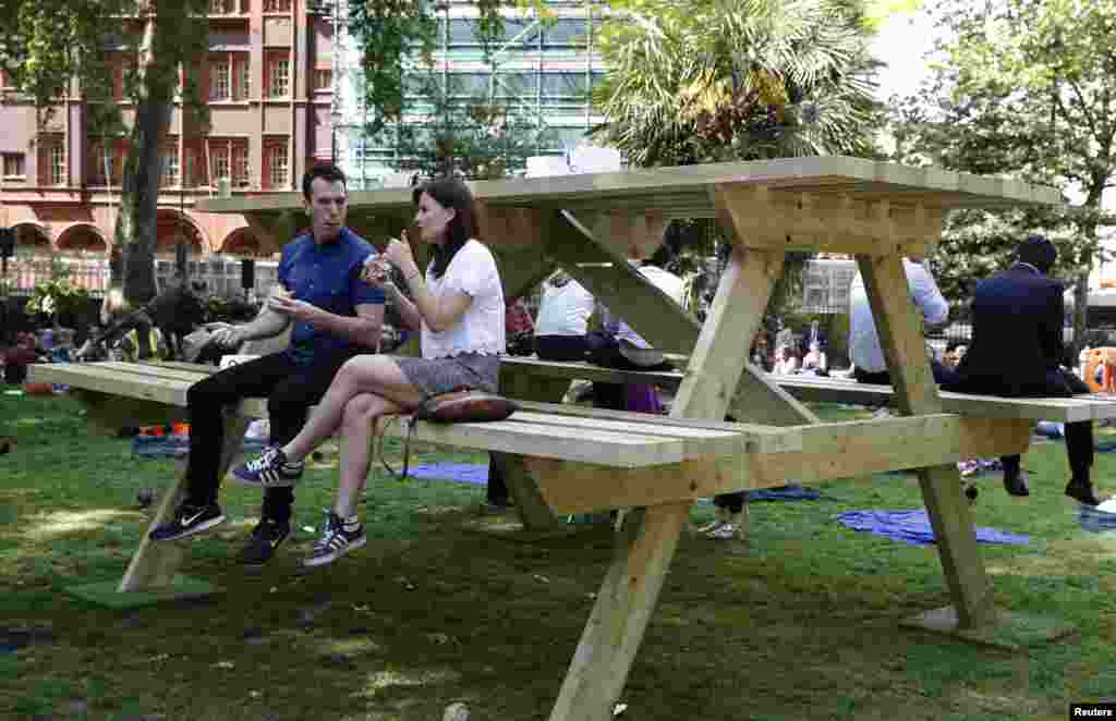 Sepasang muda-mudi duduk di atas meja piknik ukuran besar di Lapangan Soho, London.