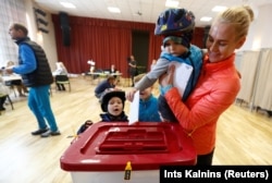 Latvia - A child casts its mother's vote during a general election in Ikskile