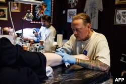 Tattoo artists ink designs on customers during a session at The Rembrandt House Museum in Amsterdam on June 19, 2023. (Photo by SIMON WOHLFAHRT / AFP)