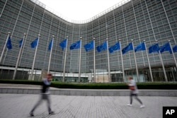 FILE - European Union flags wave in the wind as pedestrians walk by EU headquarters in Brussels, on Sept. 20, 2023. (AP Photo/Virginia Mayo, File)