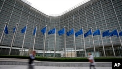 FILE - European Union flags wave in the wind as pedestrians walk by EU headquarters in Brussels, on Sept. 20, 2023. (AP Photo/Virginia Mayo, File)