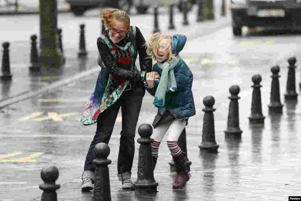 Seorang perempuan dan puterinya berjuang melawan angin kencang dan hujan yang mencapai kecepatan lebih dari 100 km per jam, di kota Brussels, Belgia. 
