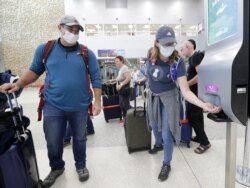 FILE - Linda Scruggs, right, applies hand sanitizer as Mike Rustici, left, watches after they arrived on a flight from Lima, Peru, March 21, 2020, at Miami International Airport in Miami.