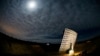 FILE - Light from a full moon is reflected off the Interstellar Light Collector (R) onto people in a moveable trailer (C) in the Sonoran desert near Three Points.