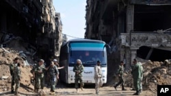 Les forces gouvernementales syriennes se rassemblent devant un bus transportant des combattants liés à al-Qaïda lors d'une évacuation du camp de réfugiés palestiniens de Yarmouk, près de Damas, en Syrie, 30 avril 2018